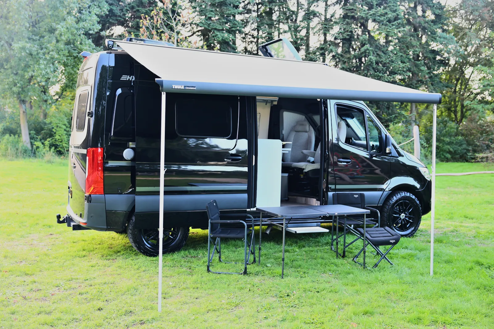 Hymer Free 600S camperbus met uitgerolde luifel, tafel en stoelen op het gras