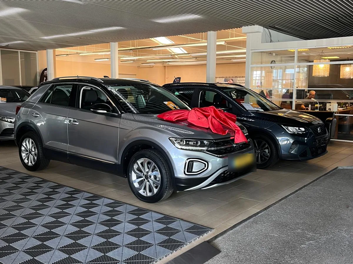 Grijze Volkswagen T-Roc met rode strik in de showroom van AVM, klaar voor aflevering aan de koper